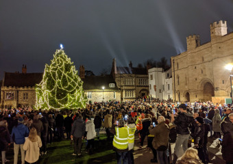 Large Christmas tree lit up with lights outside historic building by Lincoln Cathedral, with crowd of people
