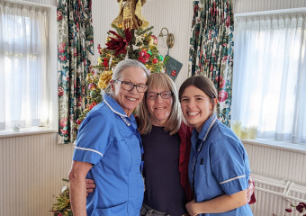 Two nurses in blue uniforms with woman wearing black in front of Christmas tree