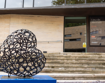 Sculpture made of horseshoes on blue plinth, outside of brick building with Lincoln Museum signage on door