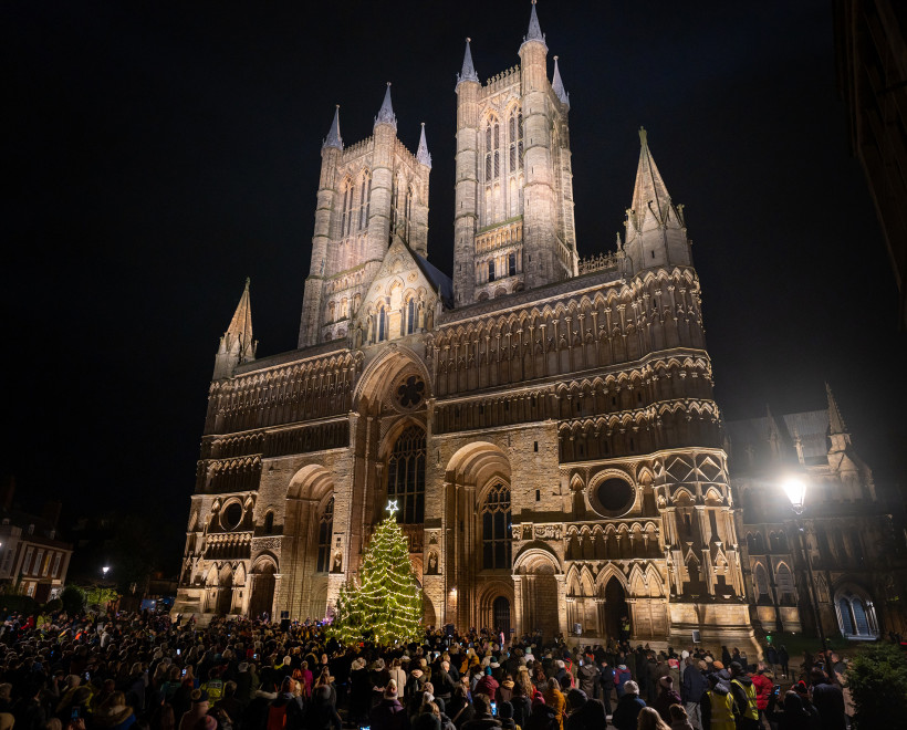 Lincoln Cathedral illuminated at night with St Barnabas Tree of Life and crowd of supporters