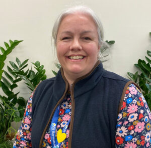Rebecca Franks, grey haired woman wearing dark blue gilet and flowery top