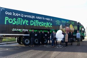 A group of people who work at Branston LTD, infront of a branded truck, alongside the heart