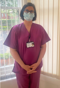Woman with short brown hair wearing pink scrubs with lanyard, blue PPE facemask.