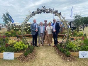 Four men in suits and blonde woman standing under archway in botanical garden at Lincolnshire Show