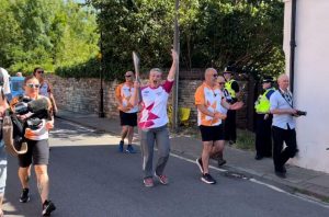 Rachael Bradley, a woman wearing a white and pink top, carrying the Queen's Relay baton through the streets of Grantham, surrounded by people