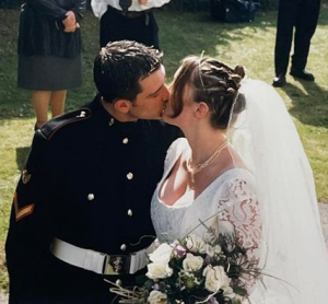 A man in black uniform and woman in white bridal gown with veil kissing on their wedding day.