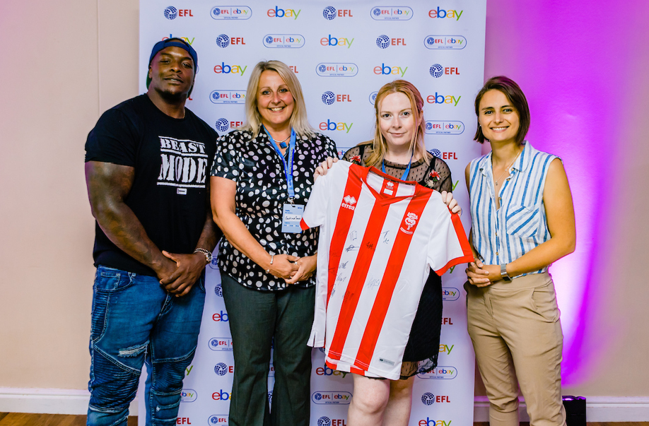 Three women and a man holding red and white striped football shirt