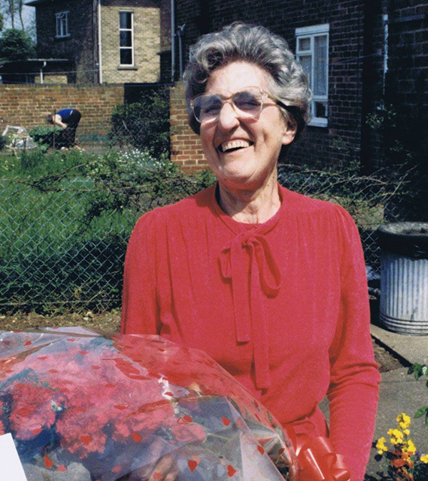 Connie Stenton, a woman with silver hair, wearing glasses and red top, holding bouquet of red roses
