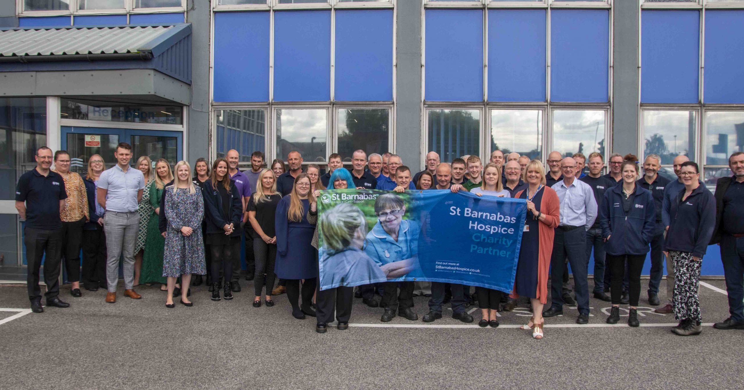 A group of people, who work for Fenner Precision and James Dawson, holding a banner in support of St Barnabas Hospice