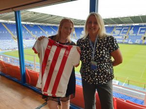 Two women, at a football stadium, holding a signed Lincoln City FC shirt.