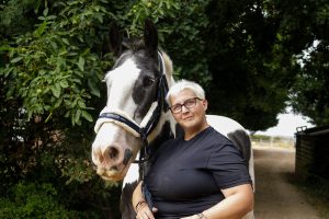 A woman with short white hair, black glasses and black top with a large white and black horse