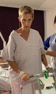Woman with short blonde hair and hospital gown holding zimmer frame