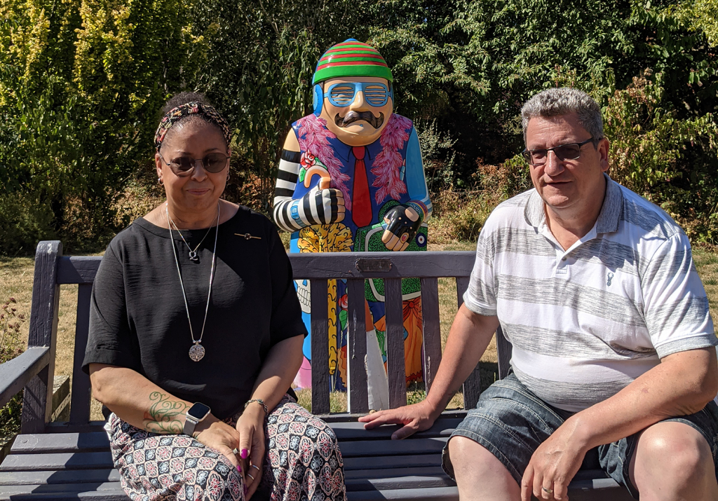 Man and woman sitting on a wooden bench with behind them a brightly coloured statue of Lincoln Baron