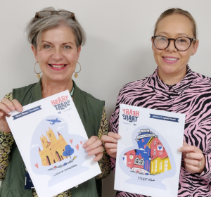 Two women holding pieces of paper with heart designs