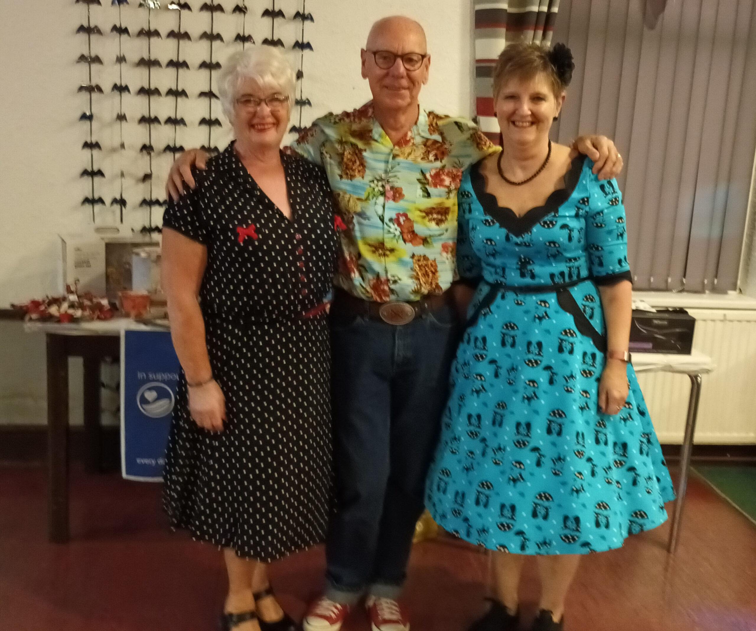 Two women in 1950s style dresses with man wearing bright shirt in the middle
