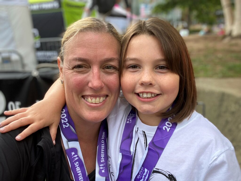 A woman and young girl smiling, both wearing purple ribbons around their necks