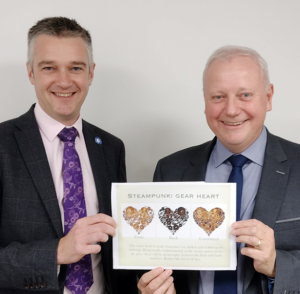 Two men in suits and tie holding paper with heart designs