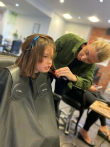 Young girl with black hairdressers smock sitting as hairdresser cuts her hair