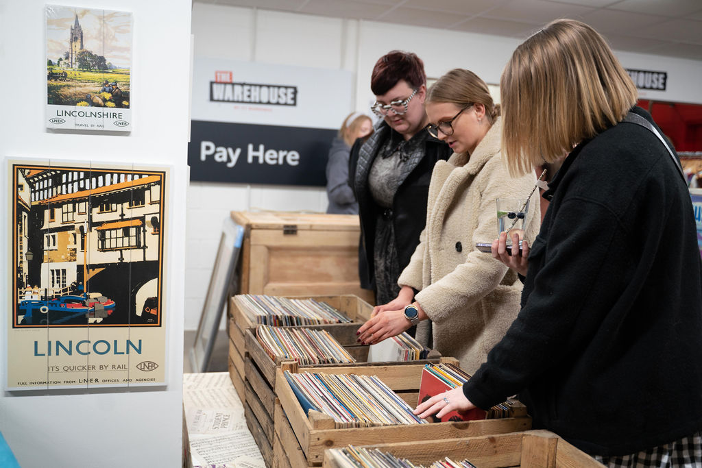 Three people standing by wooden crates filled with vinyl records