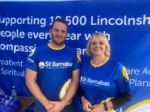 Man and blonde woman wearing blue St Barnabas Hospice tops smiling against blue backdrop with white text