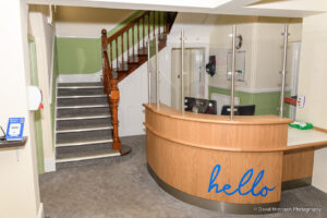 Reception area with light brown wooden desk with blue 'hello' sign and stairway with green wall