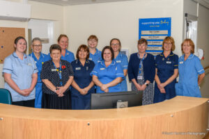 Clinical staff including nurses in blue uniforms at light brown wooden reception desk