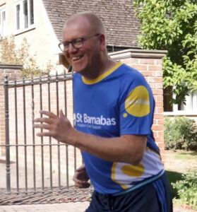 Man wearing blue top with St Barnabas Hospice branding, running and smiling