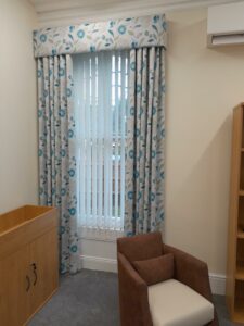 Large top to bottom window in a room with blue curtains and cosy brown chair