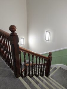 Looking down a stairway from above, with brown banisters, white and green walls and grey carpets