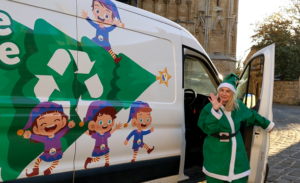 White van with illustration of Christmas tree and elves, with blonde woman wearing green elf costume opening car door