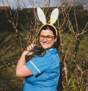 Woman in blue nurse uniform holding black rabbit, and wearing white bunny ears