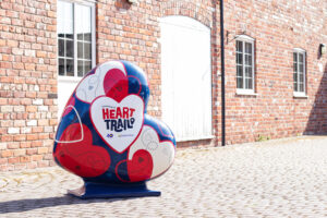 Large heart sculpture painted blue, red and white with HeART Trail logo, outside of red brick building