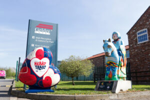 Large heart sculpture painted blue, red and white with HeART Trail logo next to painted Knight statue outside of Gelders offices