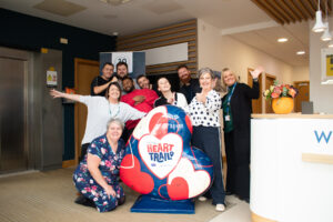 Group of people posing with a large heart sculpture painted blue, red and white with HeART Trail logo