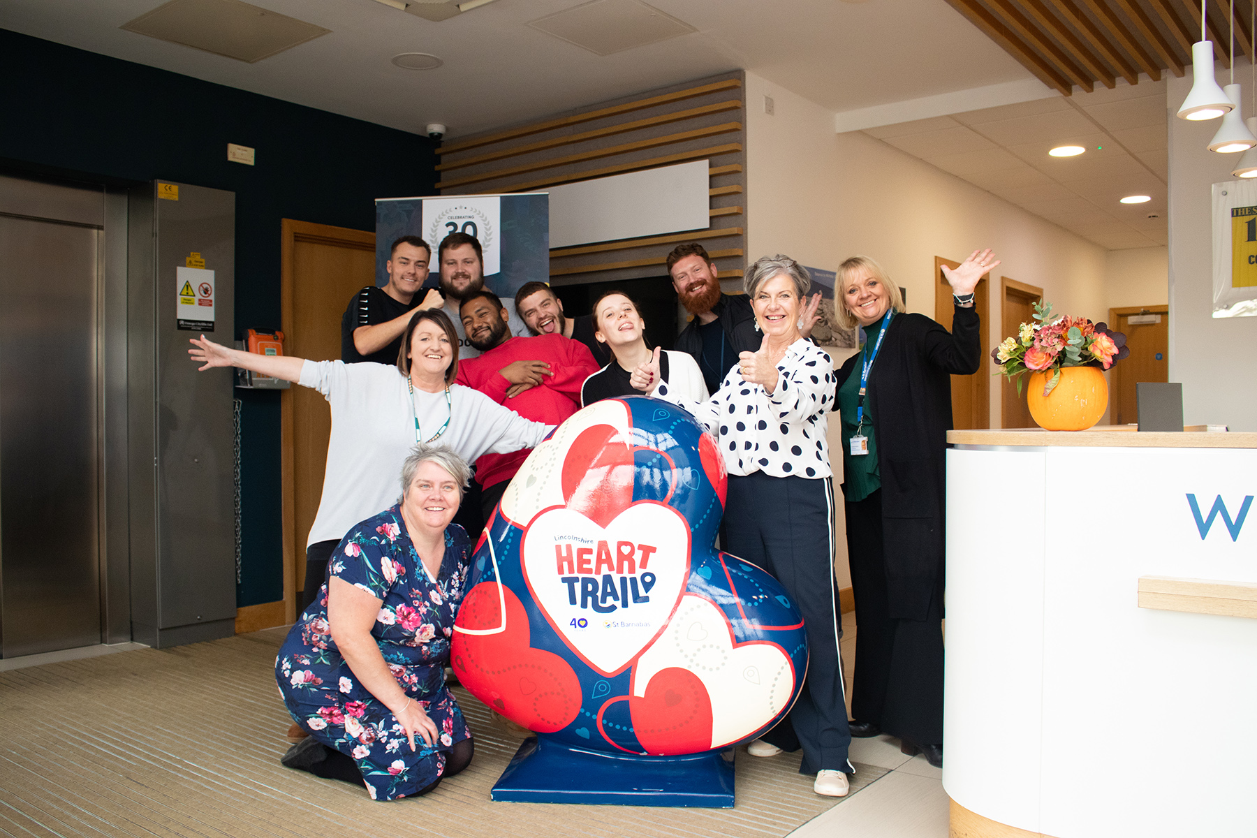 Group of people posing with a large heart sculpture painted blue, red and white with HeART Trail logo