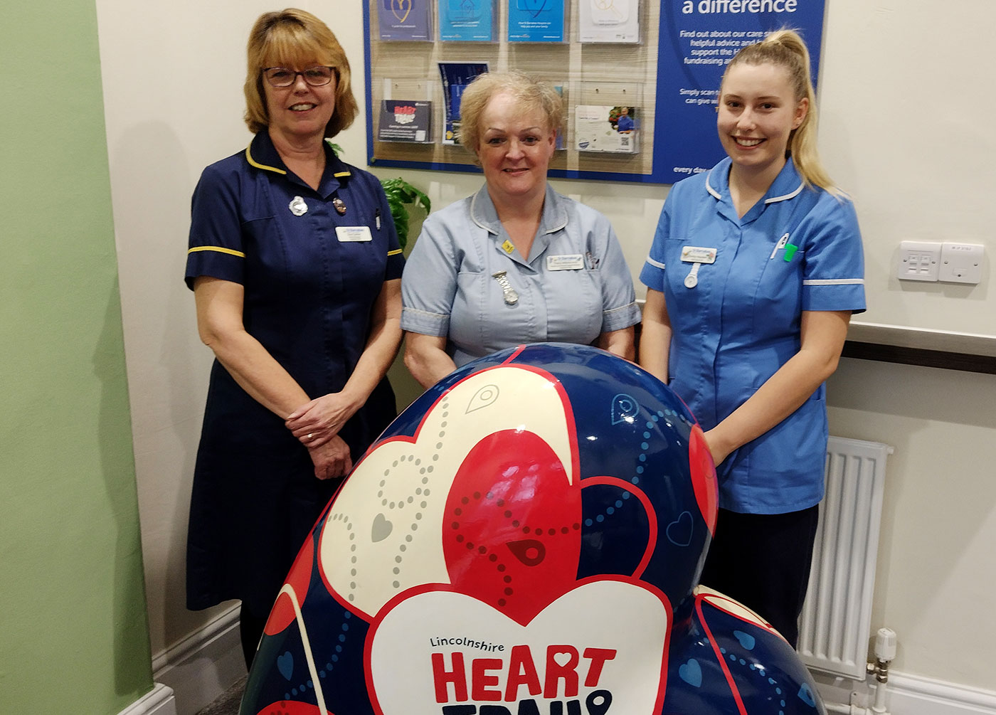 Three women in blue medical scrubs with large red, blue and white heart
