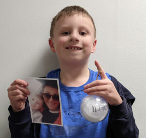 Young boy smiling while holding white Christmas bauble and photograph
