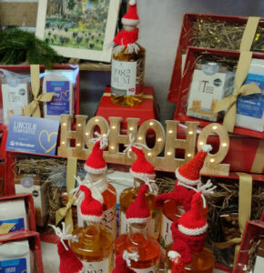 Bottles of gin and rum with knitted red Santa hats and scarves, hampers and others items around a wooden HoHoHo sign at Christmas Market stall