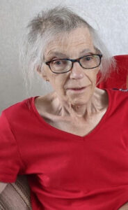 Elderly woman with silver hair, wearing black glasses and red top
