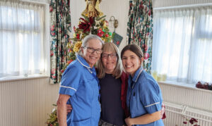 Two nurses in blue uniforms with woman wearing black in front of Christmas tree