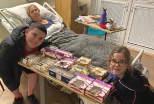 Woman in hospital bed with table full of cakes and two children