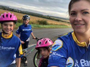 Woman and three children wearing blue St Barnabas Hospice tops, with bicycle and helmets, smiling at camera