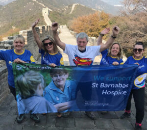 Group of people holding blue St Barnabas flag on the Great Wall of China, with blue sky and mountains in background