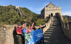 Group of people holding blue St Barnabas flag on the Great Wall of China, with blue sky and mountains in background