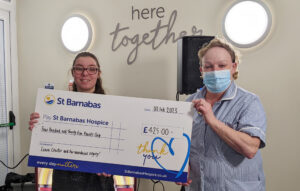 Young woman wearing glasses and older woman wearing blue facemask, they are holding a large presentation cheque for St Barnabas Hospice