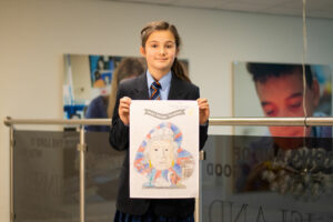 Young girl with brown hair and navy blue school uniform, holding drawing of heart shape