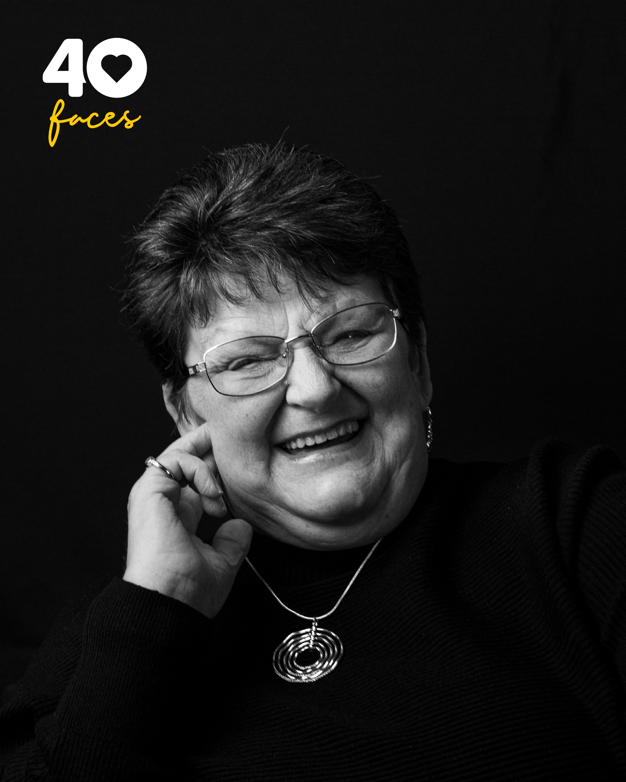 A lady, Yvonne Tye, who is a Ward Clerk at St Barnabas Hospice, photographed in black and white, against a black backdrop