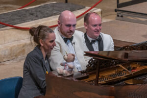 Two men in white suit jackets and a woman sitting at piano