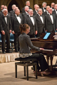 Female pianist accompanying male voice choir in black tuxedos