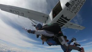 Two people skydiving in tandem, with white plane and blue sky in background